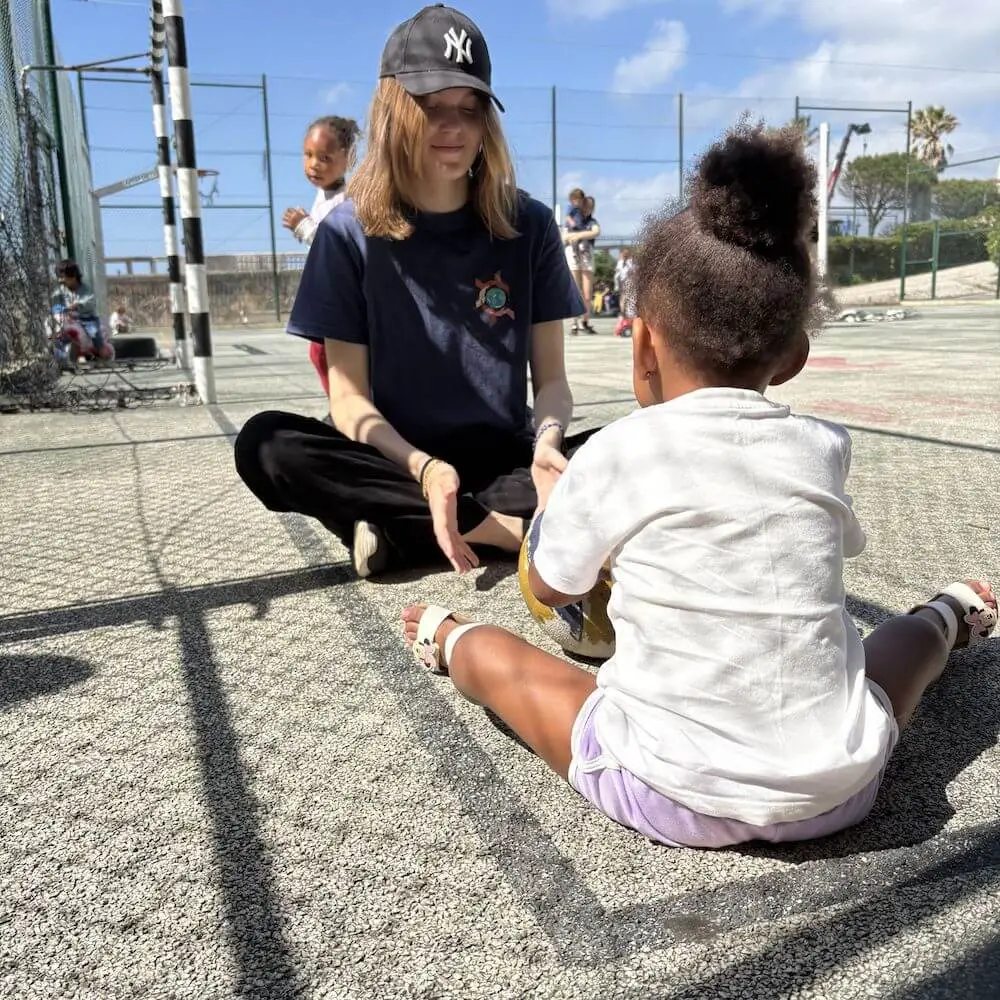 Volunteer supporting a child during an outdoor activity in Lisbon, showing the childcare and community support focus of Abroad Escape volunteer programs in Portugal.